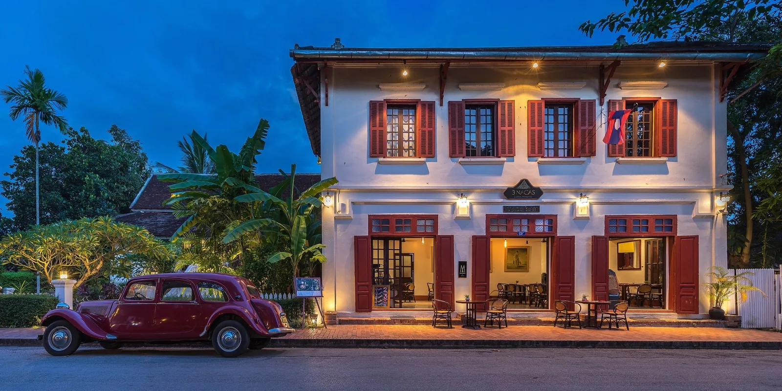 A vintage red car sits before a French colonial hotel lit up at dusk in Luang Prabang.