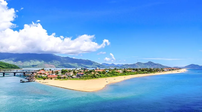 Aerial view of Lang Co Beach's narrow sandy peninsula between blue sea and lagoon, backed by mountains near Hue.
