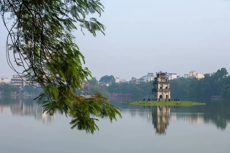 Turtle Tower stands on a small island in Hoan Kiem Lake, framed by hanging tree branches in Hanoi.