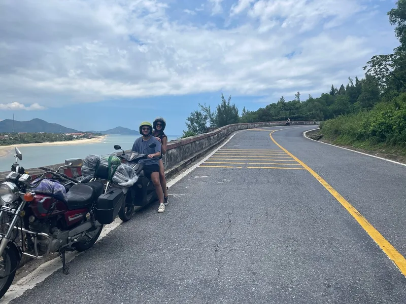 Two travelers pause on a loaded motorbike overlooking the coast along the winding Hai Van Pass.