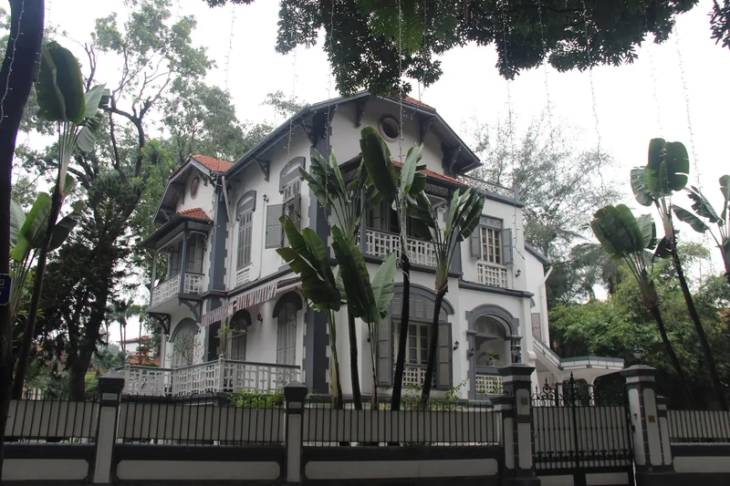A French colonial-era mansion with grey shutters and terracotta roof tiles stands behind a fence in Hanoi.