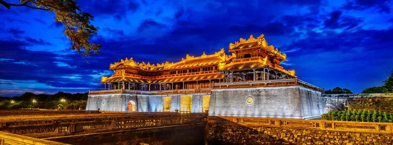 The Meridian Gate of Hue Imperial City glows golden against a dramatic blue twilight sky.