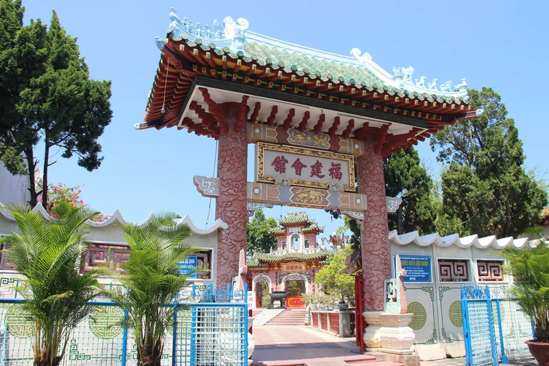 Ornate red and gold gate of the Fujian Chinese Assembly Hall in Hoi An under a clear blue sky.