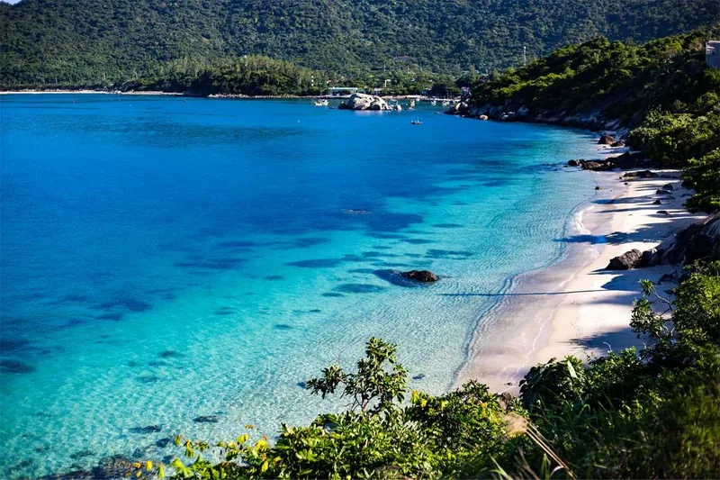 Turquoise water and a white sand beach curve around a forested hillside on Cham Island, Vietnam.