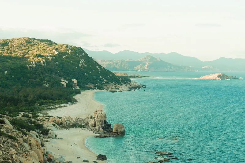 A rocky coastline curves along turquoise waters with mountains in the distance in Ninh Thuan.