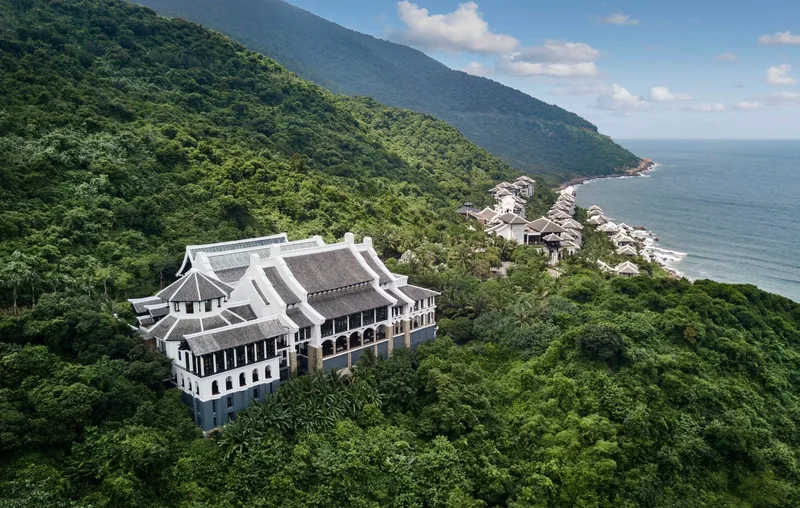 An elegant resort building sits amid green mountainside forest overlooking the coastline near Da Nang.