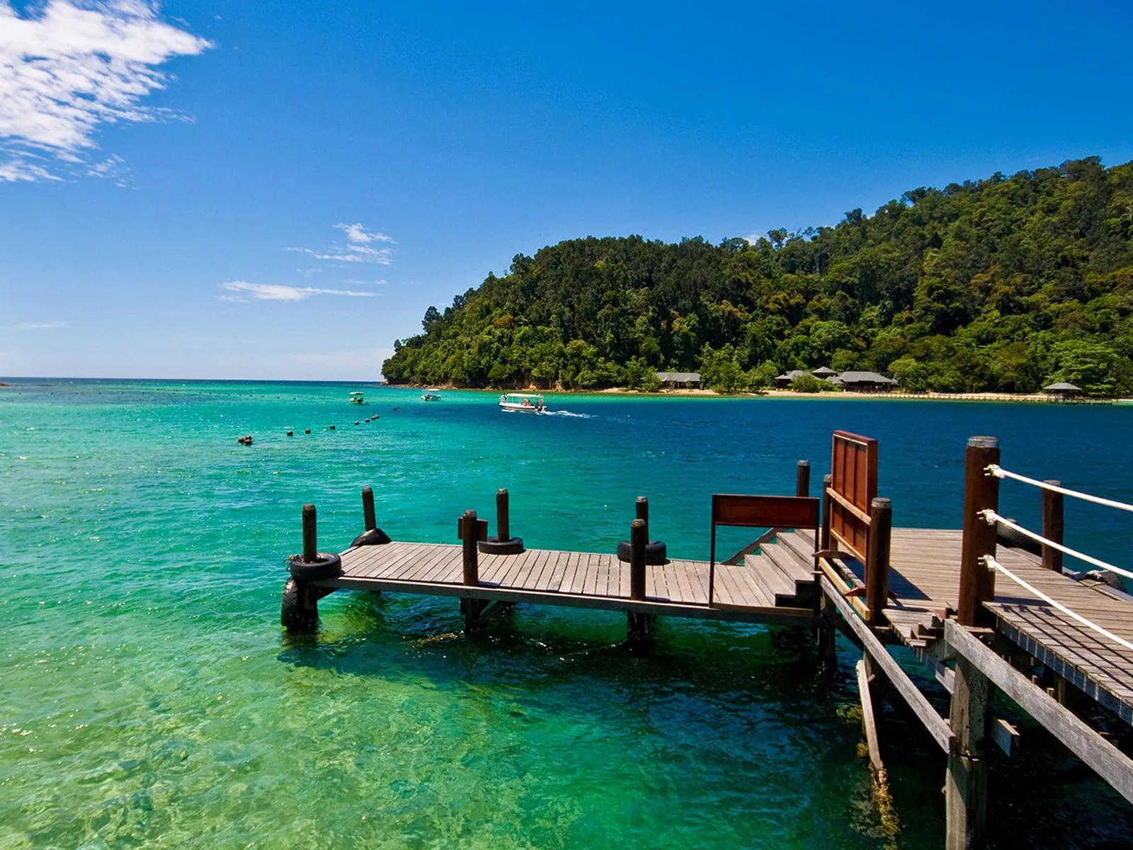 A wooden pier extends into turquoise waters near a forested coastline in central Vietnam.