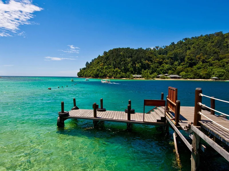 A wooden pier extends into turquoise waters near a forested coastline in central Vietnam.