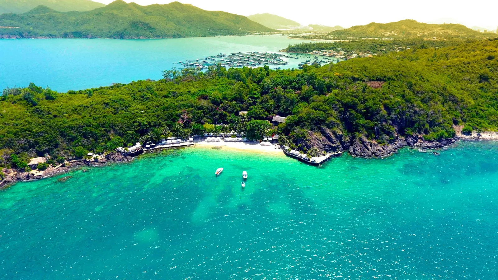 Aerial view of a small resort beach with turquoise water and boats along a forested coastline near Nha Trang.
